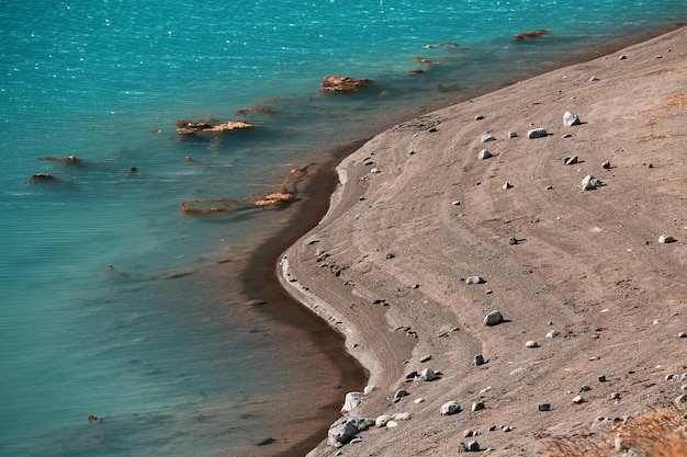 Die Textur der Küste. Türkisfarbenes Meerwasser und Ufer mit Sand und Steinen.