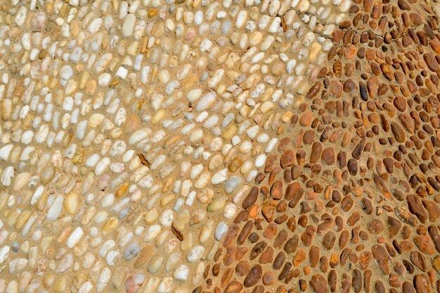 Die Textur der Steinmauer der Straße aus kleinen runden und ovalen Steinen mit abstrakten Linien