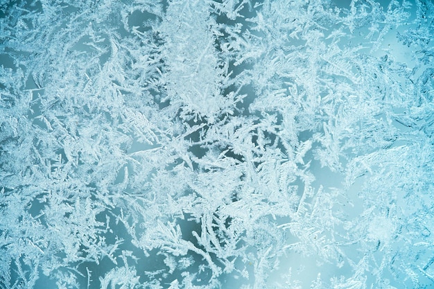 Die Textur ist gefrorenes Glas, der Hintergrund des Frostmusters ist blau. Schneeflocken auf dem Glas