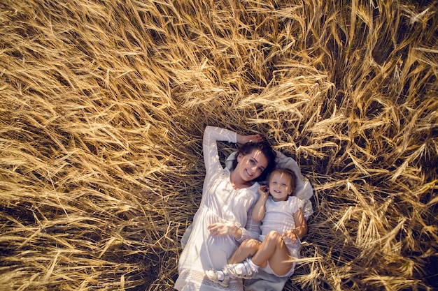 Die Tochter mit der Mutter liegt abends im Sommer mit Ohren auf dem Boden auf dem Feld