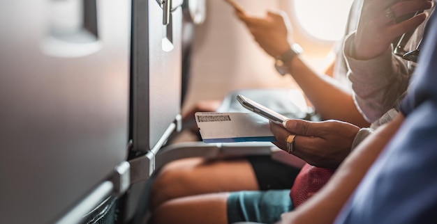 Die Touristen, die telefonieren und ein Ticket in dem Flugzeug zur Hand haben, das sich auf den Start vorbereitet. Flugzeug, Reisen, Smartphone, Flughafen, Ticket, Technologiekonzept.