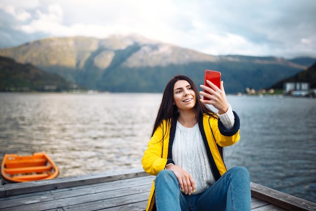 Die Touristin macht ein Foto am Telefon am See in Norwegen Junge Frau macht Selfie