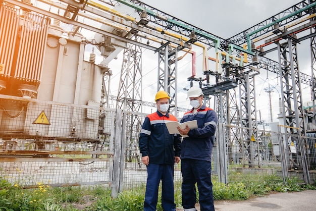 Die Umspannwerke der Ingenieure führen abends zur Zeit der Pandämie eine Untersuchung moderner Hochspannungsgeräte in der Maske durch. Energie. Industrie.