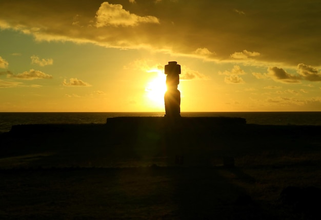 Die untergehende Sonne scheint durch Moais Silhouette bei Ahu Tahai, Osterinsel, Chile