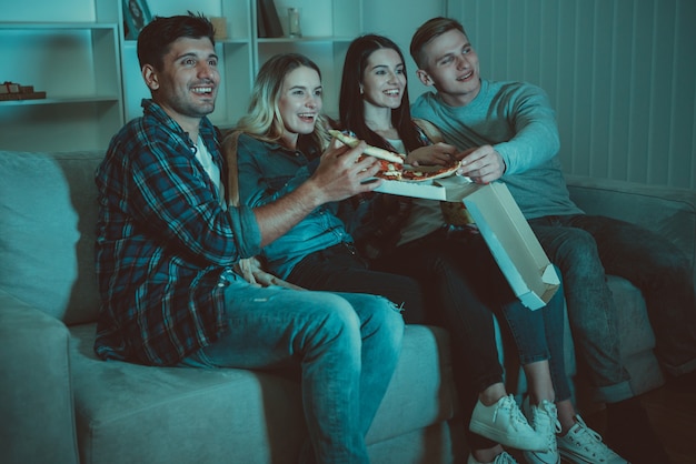 Die vier Leute essen eine Pizza und schauen sich auf dem Sofa einen Film an