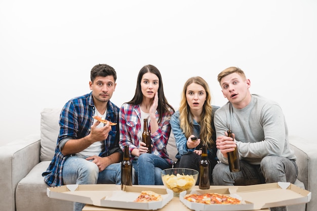 Die vier Leute schauen mit einer Pizza und einem Bier auf dem weißen Hintergrund fern