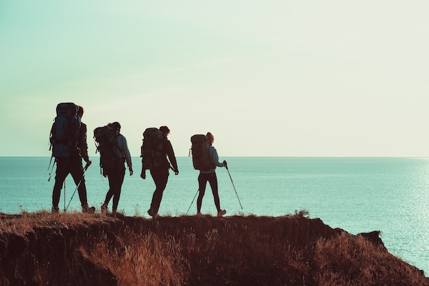 Die vier Reisenden mit Rucksäcken, die auf dem Berggipfel in der Nähe des Meeres spazieren gehen