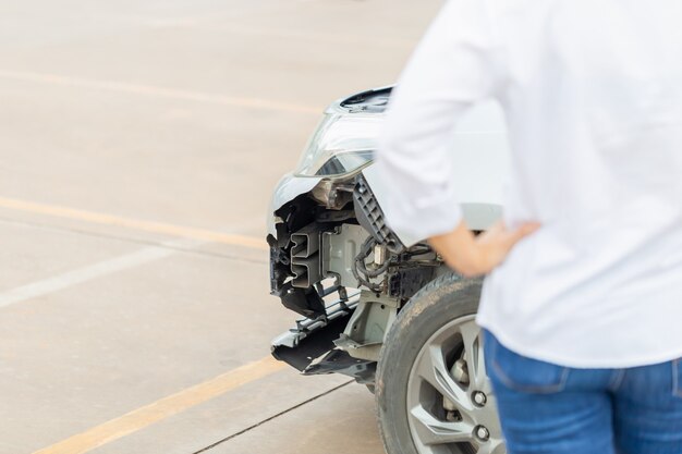 Die Vorderseite des Autos wird beschädigt, während eine junge Frau nach einem Autounfall am beschädigten Auto steht