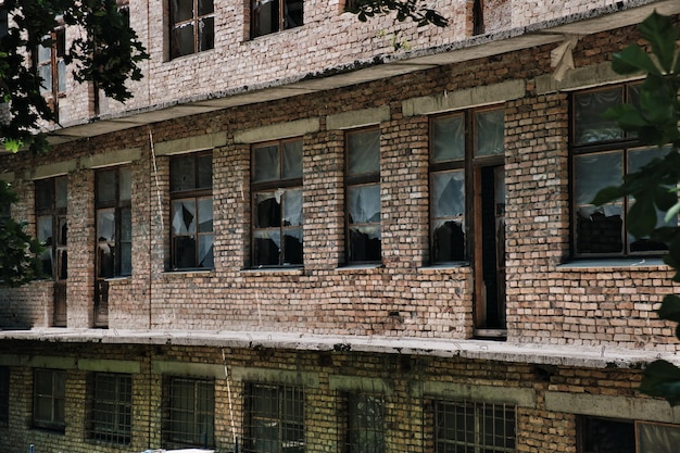 Die Wand eines alten verlassenen Backsteingebäudes mit zerbrochenen Fenstern
