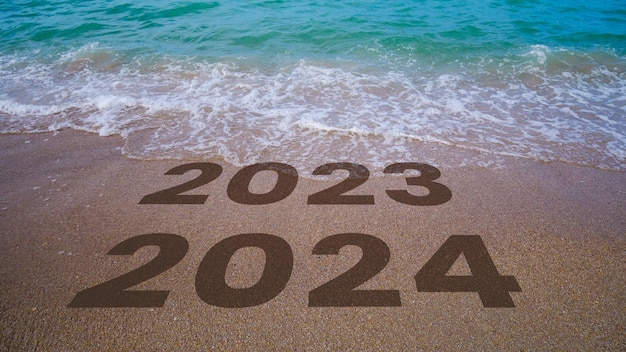 Die Wellen löschen 2023 bis 2024 aus, die am Strand in den Sand geschrieben sind: 2024