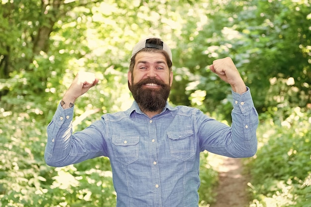 Die Welt gehört Ihnen zu erkunden Modeporträt eines bärtigen Mannes, reifer Mann mit Hut, glücklicher Hipster-Reisender, der allein im Wald im Freien steht, mit Sonnenuntergang, Natur im Hintergrund