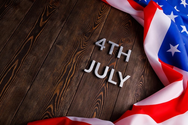 Die Worte 4. Juli und zerknitterte US-Flagge auf flachem, strukturiertem Holzoberflächenhintergrund