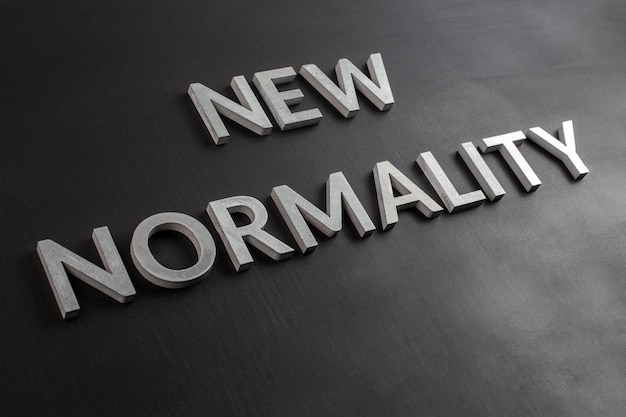 Die Worte neue Normalität mit silbernen Metallbuchstaben auf einer flachen schwarzen, matten Oberfläche in schräger Diagonalperspektive