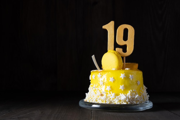Die Zahl Neunzehn auf einem gelben Kuchen zum Jubiläum oder Geburtstag in einem dunklen Schlüssel