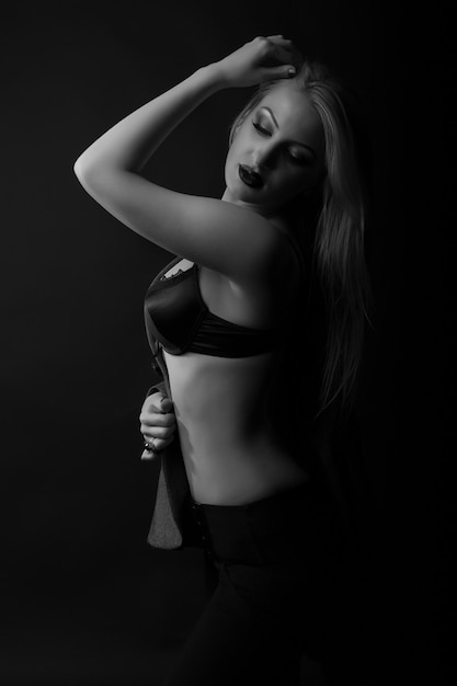 Die zarte junge Dame trägt einen BH, der im dunklen Studio posiert. Monochrome Aufnahme