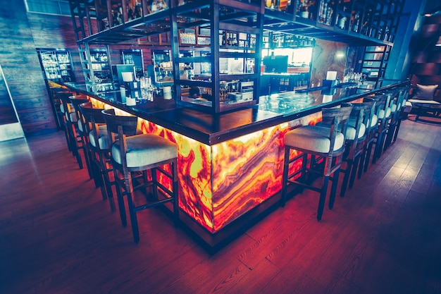 Die zeitgemäße Bartheke mit der Ausstattung und den bequemen Barstühlen im modernen Restaurant. Stilvolle Inneneinrichtung. Die dunkelblaue und rote Farbkombination.