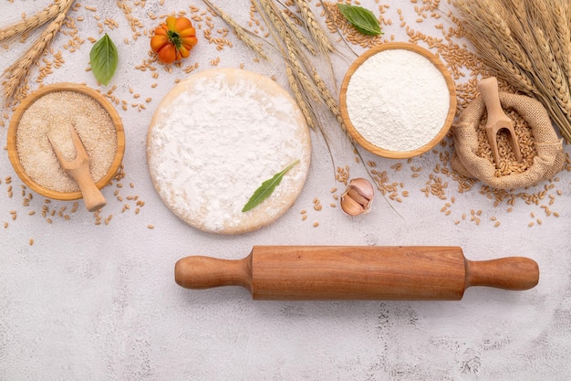 Foto die zutaten für hausgemachten pizzateig mit weizenmehl und weizenkörnern auf weißem betongrund