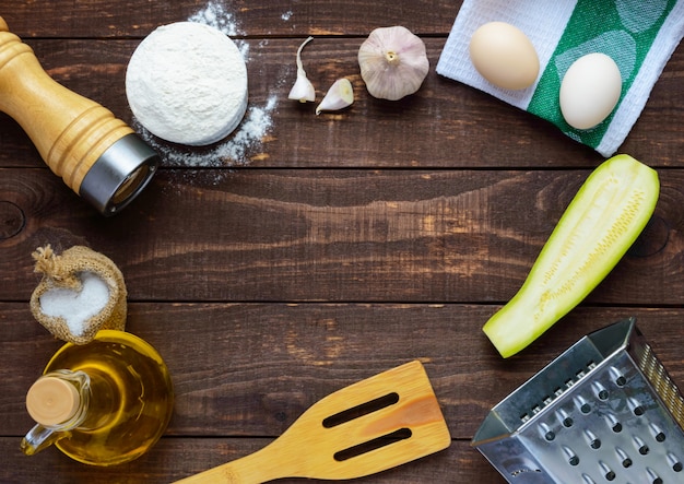 Die zutaten und werkzeuge zum kochen von pfannkuchen aus zucchini auf einem dunklen holztisch. draufsicht. in der mitte des freien platzes für text