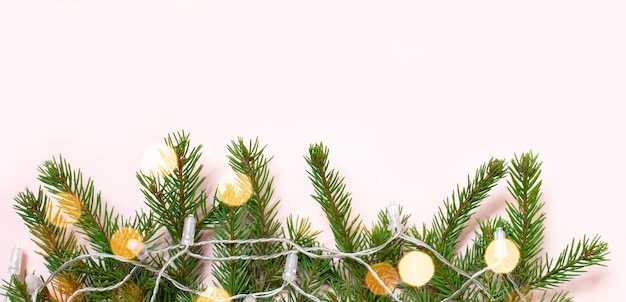 Die Zweige des Weihnachtsbaums mit Weihnachtsbeleuchtung, Bokeh. auf einem rosa Hintergrund.