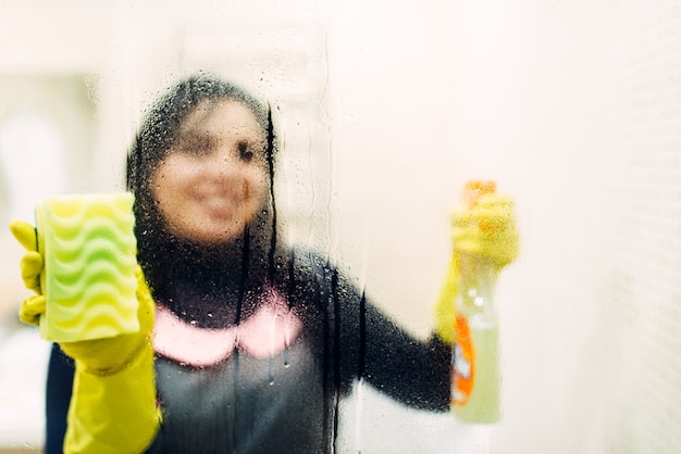 Dienstmädchen in Handschuhen reinigt Glas mit einem Reinigungsspray