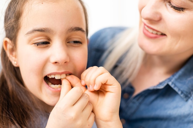 Un diente de leche suelto se cae en una niña con la boca abierta.