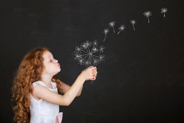 Foto diente de león que sopla de la niña con el dibujo en la pizarra.