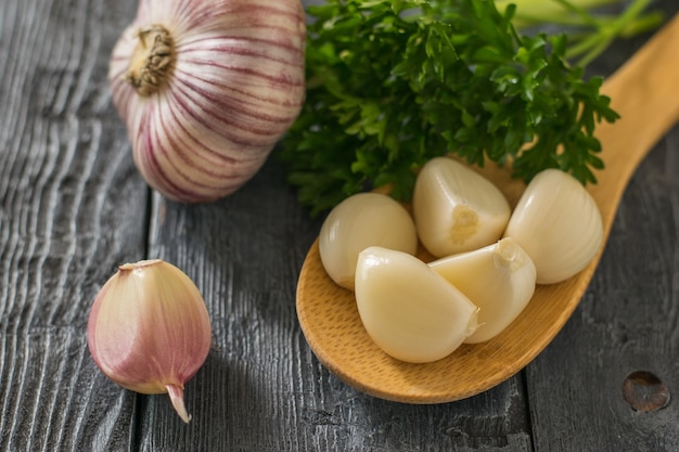 Dientes de ajo pelados en una cuchara de madera y un ajo entero sobre una mesa de madera negra. Condimento natural saludable. Componente de la medicina tradicional.