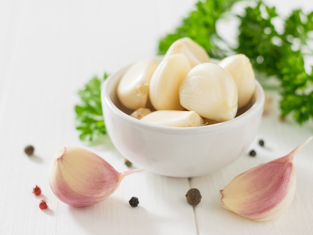 Dientes de ajo pelados en un recipiente blanco con especias sobre una mesa de madera. Condimento natural saludable. Componente de la medicina tradicional.