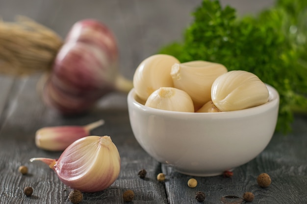 Dientes de ajo en un recipiente blanco y ajo sin pelar sobre la mesa. Condimento natural saludable. Componente de la medicina tradicional.