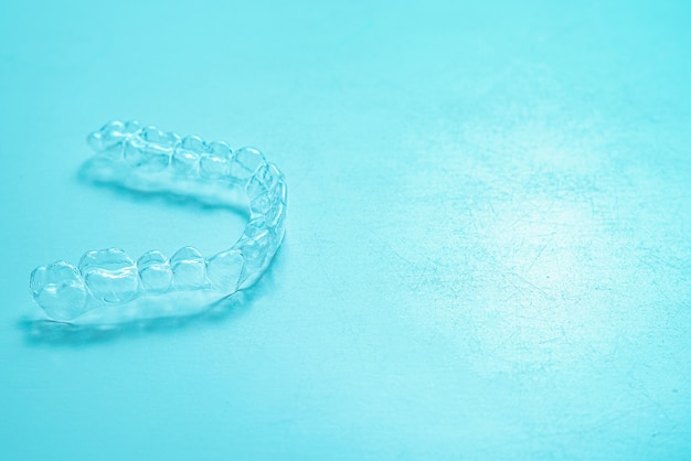 Los dientes dentales invisibles brackets alineadores de dientes sobre fondo turquesa. Frenos de plástico retenedores de odontología para enderezar los dientes.