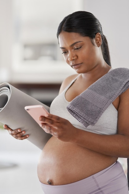 Diese Fitness-App war während meiner gesamten Schwangerschaft großartig Aufnahme einer schwangeren Frau, die ihr Handy benutzt, während sie ihre Yogamatte zu Hause hält