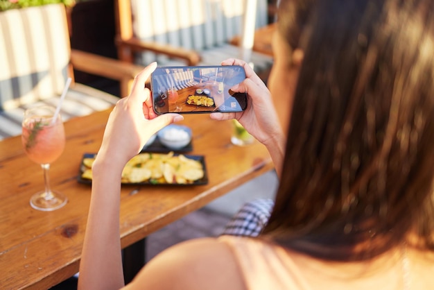 Diese schmierigen Cheatdays. Rückansicht einer nicht erkennbaren Frau, die in einem Restaurant draußen ein Bild von ihrem Essen spricht.