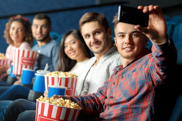 Dieser ist für eine gute Erinnerung. Gruppe glückliche nette Freunde, die das selfie zusammen sitzt in einem lokalen Kino nehmen