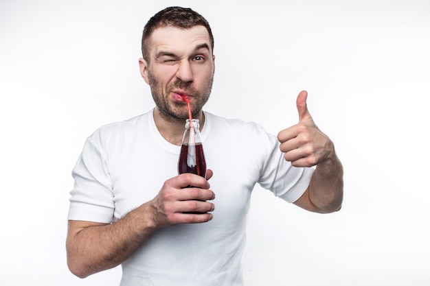 Dieser Mann mag Fast Food sehr und auch süße Getränke. Er trinkt genüsslich Cola aus der Flasche. Auch junger Kerl hält seinen großen Daumen hoch. Isoliert auf weißem Hintergrund