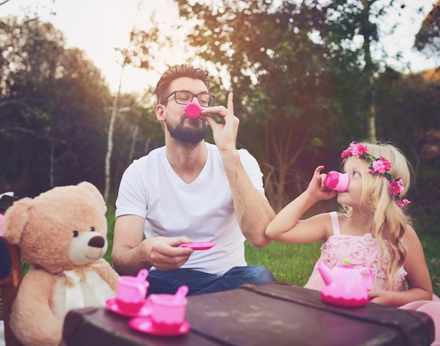 Dieser Tee ist großartig Aufnahme einer fröhlichen Tochter und eines fröhlichen Vaters bei einer Teeparty mit einem Haufen ausgestopfter Spielsachen mitten in einem Garten