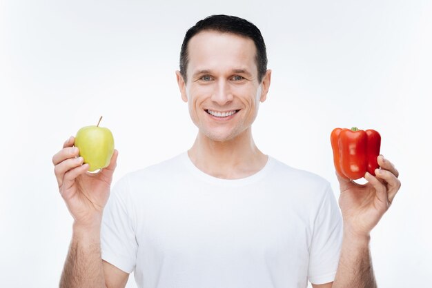 En una dieta. Alegre agradable feliz msn sonriendo y mirándote mientras te muestra comida saludable