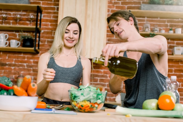 Dieta, alimentación saludable, estilo de vida físico, nutrición adecuada. Pareja consciente de salud cocinar una cena baja en calorías en la cocina del hogar. Un hombre vierte aceite de oliva en una ensalada.