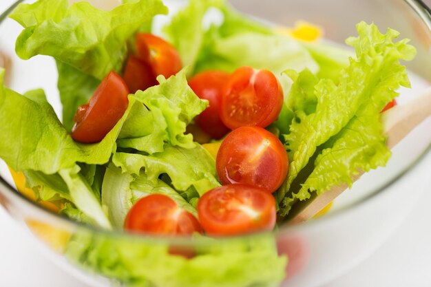 dieta, comida vegetal, alimentación saludable y concepto de objetos: cierre de ensalada de verduras con tomate cherry y lechuga en tazón de vidrio