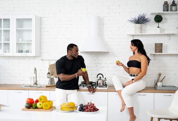 Dieta y concepto de comida saludable Hermosa mujer joven sentada cerca de un hombre multirracial en la cocina con manzana en las manos y charlando