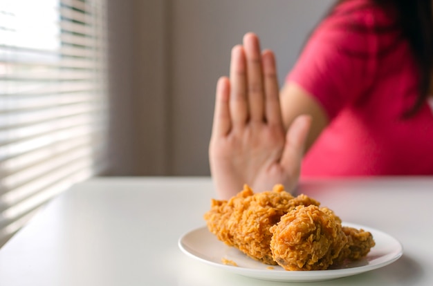 Dieta. corpo magro de mulher na camisa vermelha recusar delicioso frango frito quente na mesa para uma boa saúde em casa, junk food ou alimentos pouco saudáveis, perda de peso, estilo de vida saudável, alimentação saudável e conceito de dieta