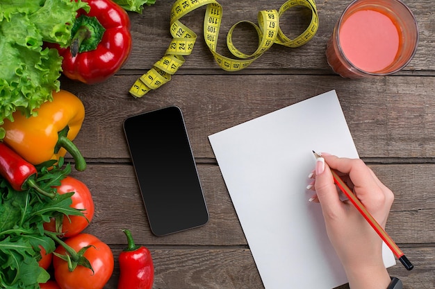 Foto dieta de conceito, plano de emagrecimento com vista superior de legumes simulado. uma mão feminina em uma pulseira esportiva escreve um artigo sobre nutrição adequada