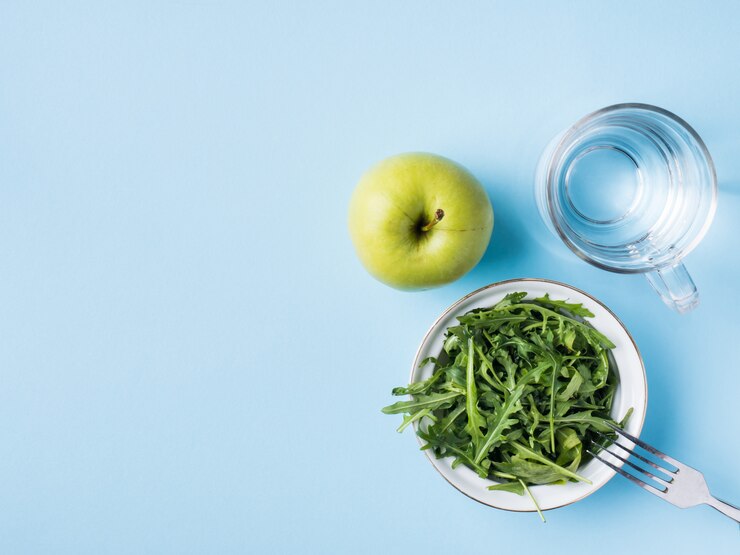 La dieta deja a Apple verde de la ensalada al vidrio de agua en fondo azul.