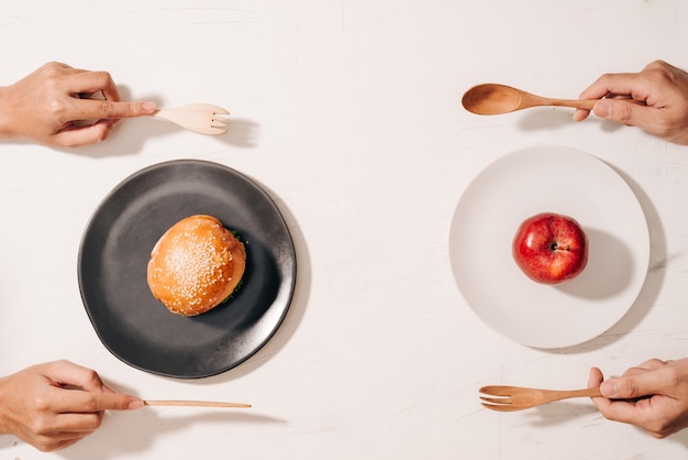 Dieta luta e decisão entre o dilema de escolha de nutrição entre frutas e vegetais frescos saudáveis ou fast food rico em colesterol competindo para decidir o que comer bolo de mãos e escolha de maçã