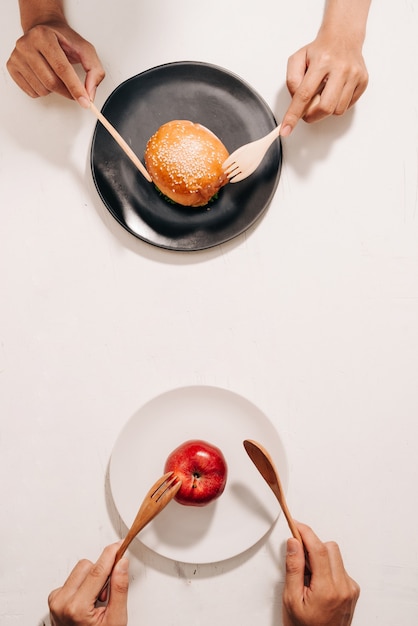 Dieta luta e decisão entre o dilema de escolha de nutrição entre frutas e vegetais frescos saudáveis ou fast food rico em colesterol competindo para decidir o que comer bolo de mãos e escolha de maçã