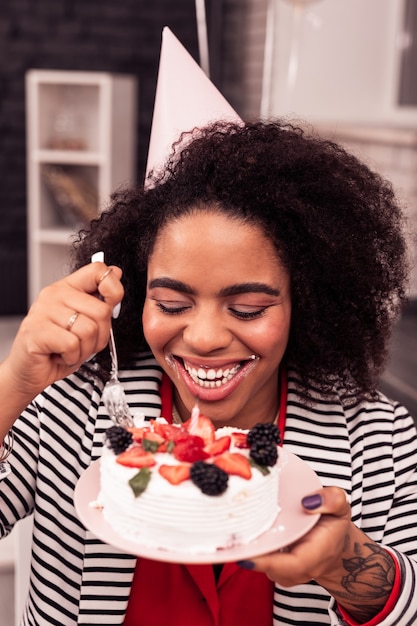 Sin dieta. Mujer hambrienta positiva sonriendo mientras sostiene un plato con un delicioso pastel