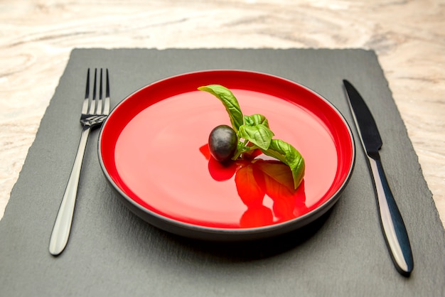 Dieta. Pequeña cantidad de comida en el plato. Una aceituna está en un plato rojo, un cuchillo y un tenedor. Concepto de dieta y pérdida de peso. Espacio vacío para texto.