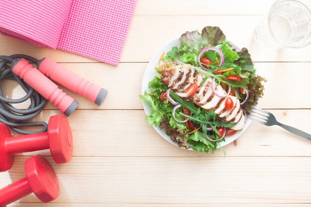 Dieta plana y concepto de fitness. Ensalada saludable y equipos de fitness en la mesa.