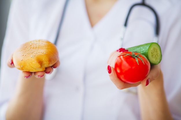 Dieta. Primer plano de mujer médico dando una elección entre empanada y verduras frescas