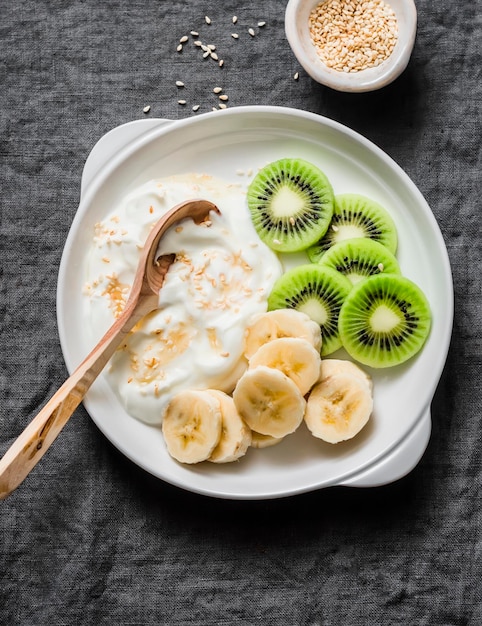 Dieta saludable desayuno yogur griego con miel y plátano y kiwi sobre un fondo gris