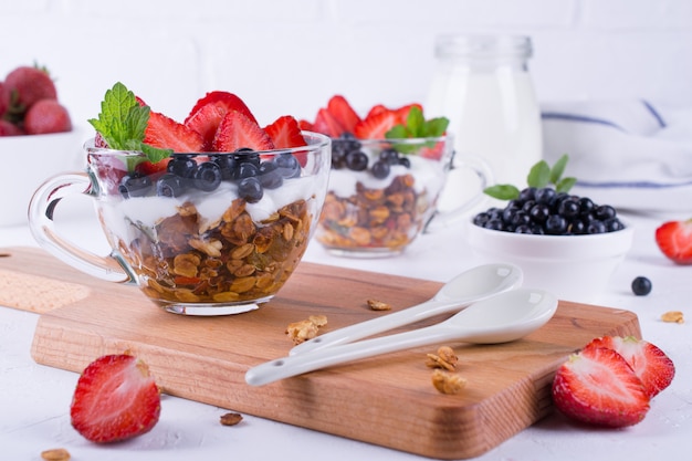 Foto dieta saludable postre con yogurt, granola y bayas frescas. en el fondo de la mesa blanca